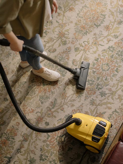 Close-up view of a beige, plush carpet in a residential room, showing a clean surface with a soft, dense pile that appears freshly vacuumed or deep cleaned, with a subtle sheen from lighting. The carp