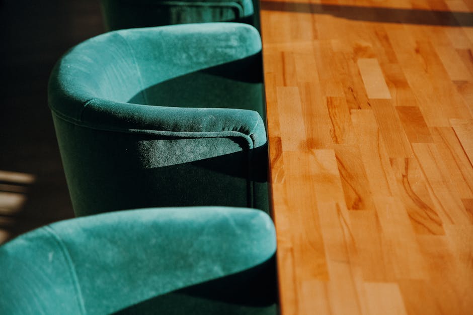 A person using a handheld electric upholstery cleaner on a dark gray fabric sofa in a living room, with the device pressed into the cushion to remove dirt. The sofa is positioned next to a Christmas t